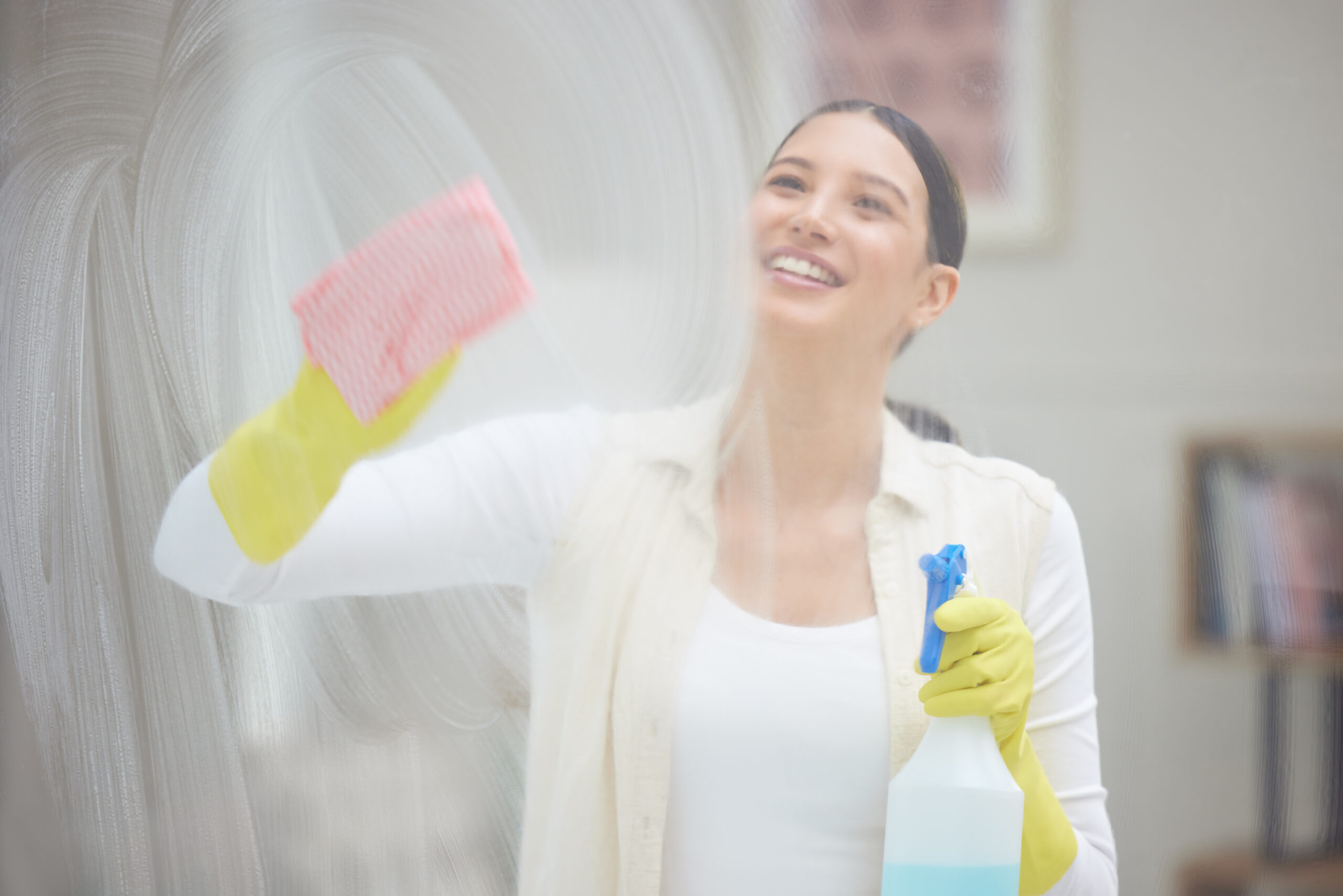 Shot of a young woman cleaning a window in her home.
